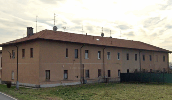 Edificio residenziale con tetto in tegole e antenne, visto da una strada."