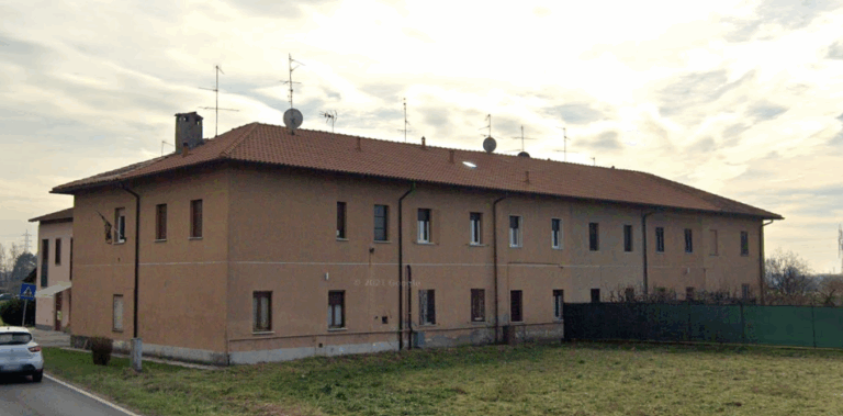Edificio residenziale con tetto in tegole e antenne, visto da una strada."
